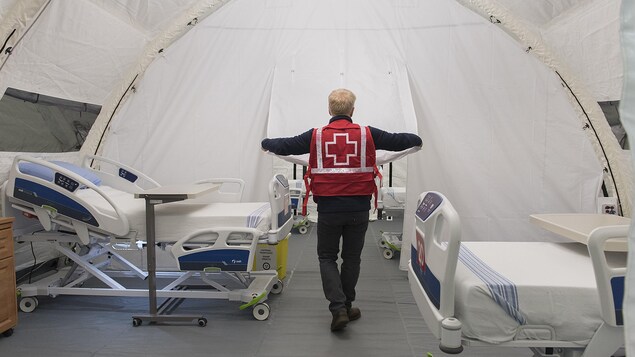 Un employé de la Croix-Rouge vu de dos dans une chambre avec deux lits.