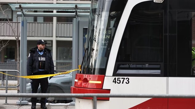 Un agent de la Commission de transport de Toronto est debout près un ruban jaune.