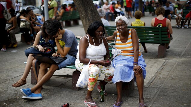 Des Cubains assis dans un parc utilisent des ordinateurs portables ou des téléphones cellulaires. Des Cubains assis dans un parc utilisent des ordinateurs portables ou des téléphones cellulaires.