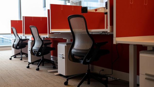 Une suite de cubicules identiques, séparés par des panneaux, avec une chaise de bureau vide, dans un bureau vide.