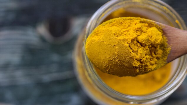De la poudre de curcuma dans une cuillère en bois. De la poudre de curcuma dans une cuillère en bois.