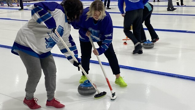 Deux joueuses de curling jouent sur la glace. 