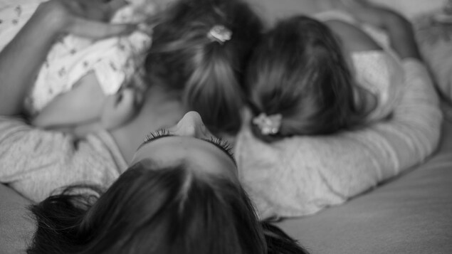 Une mère est couchée sur le dos, ses deux filles collées sur sa poitrine. Une mère est couchée sur le dos, ses deux filles collées sur sa poitrine.