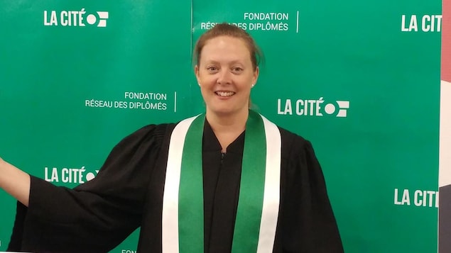 Une jeune dame habillée d'une toge devant une banderole portant le logo du collège La Cité, à Ottawa.