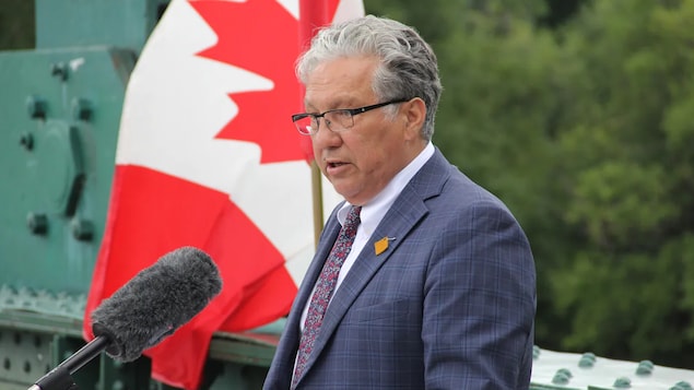 Le ministre des Affaires du Nord, Dan Vandal, est debout devant un microphone et à côté d'un drapeau canadien lors de son annonce concernant des logements aux Métis des Territoires du Nord-Ouest.