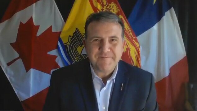 Daniel Allain en pleine entrevue vidéoconférence. Derrière lui, des drapeaux du Canada, de l’Acadie et du Nouveau-Brunswick.