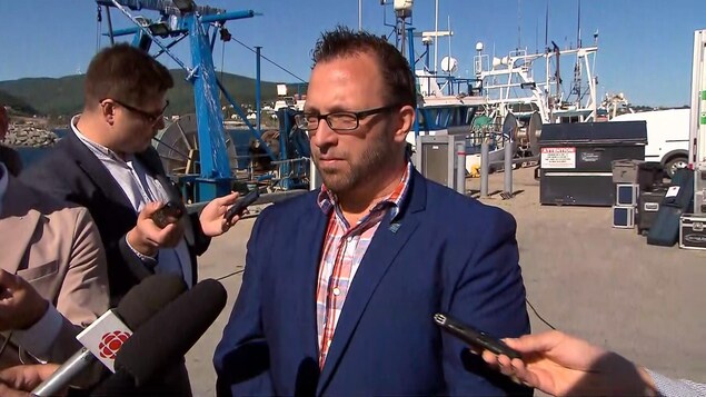 Daniel Côté répond aux questions de journalistes devant un bateau de pêche. Daniel Côté répond aux questions de journalistes devant un bateau de pêche.