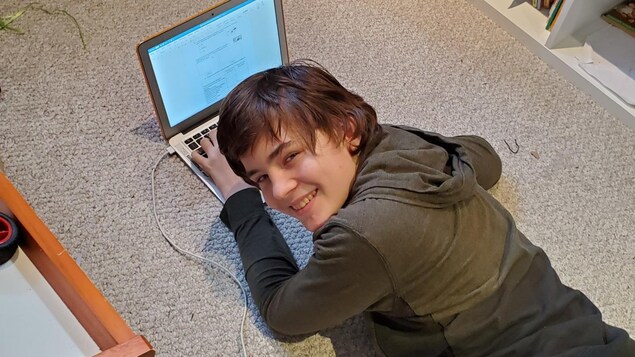 Daniel Harvey souriant est allongé sur un tapis beige devant un ordinateur portable.