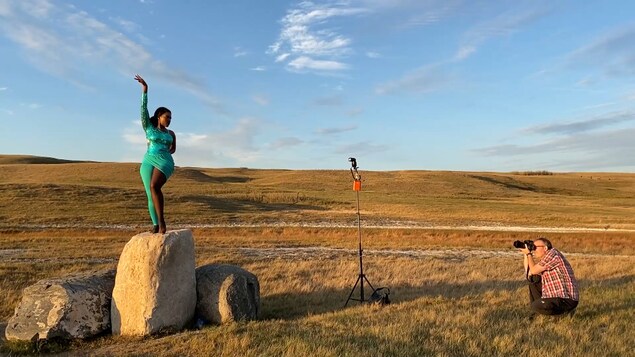 Le photographe Daniel Paquet prend en photo la danseuse Flany Ba. Flany danse debout sur une roche au milieu d'une vallée.