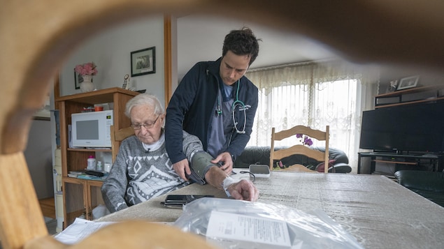 L'infirmier prend la pression d'un patient dans la salle à manger de ce dernier.