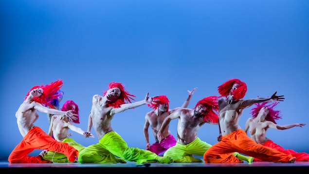 Des danseurs et des danseuses torse nu, portant des pantalons colorés, sur un fond bleu.