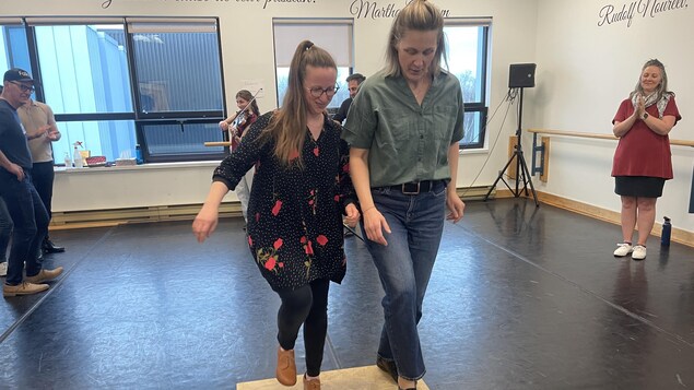 Deux femmes dansent ensemble sur une plaque en bois, d'autres les regardent.