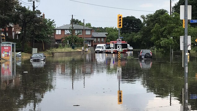 Des véhicules tentent de circuler sur une rue inondée. 