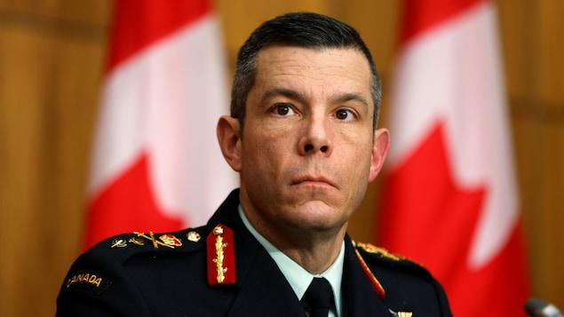 الميجور جنرال داني فورتان في مؤتمر صحفي وخلفه أعلام كندية.