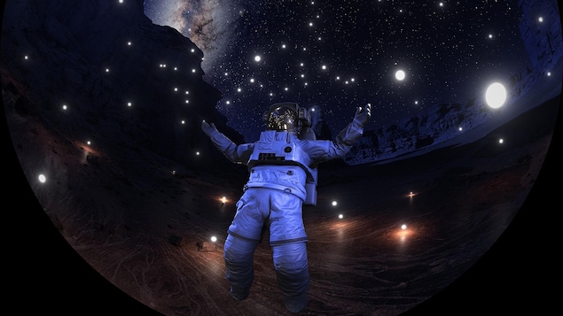 Un homme en tenue d'astronaute se tient devant un ciel étoilé où l'on peut apercevoir une galaxie au loin. 