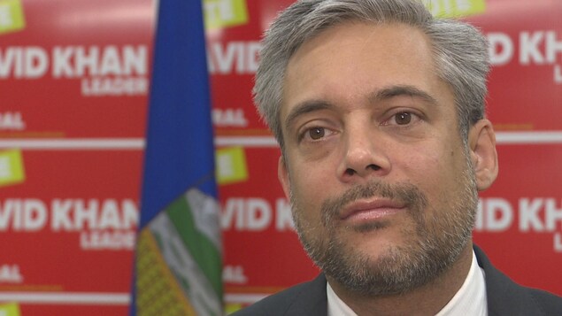Le chef du Parti libéral de l'Alberta, David Khan, derrière un drapeau et des pancartes dans son bureau à Calgary.