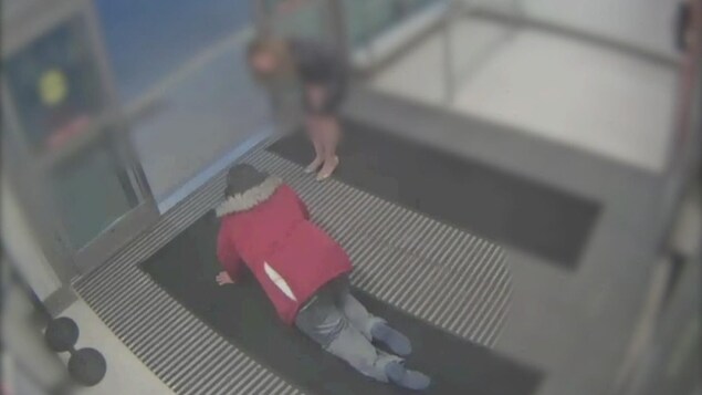 Une homme portant un manteau rouge marche à quatre pattes vers une sortie. Une femme se tient près de lui.