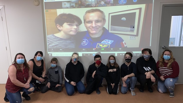 Jeunes et animatrices posent près de mur où se trouve David Saint-Jacques par visioconférence.