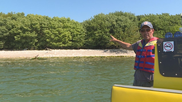 Un homme avec une ceinture de sauvetage sur un bateau pointe une île en expliquant des choses. Un homme avec une ceinture de sauvetage sur un bateau pointe une île en expliquant des choses.