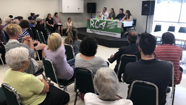 Les quatre candidats sont assis à une table, devant des dizaines de personnes. Harold Lebel parle au micro. Les quatre candidats sont assis à une table, devant des dizaines de personnes. Harold Lebel parle au micro.