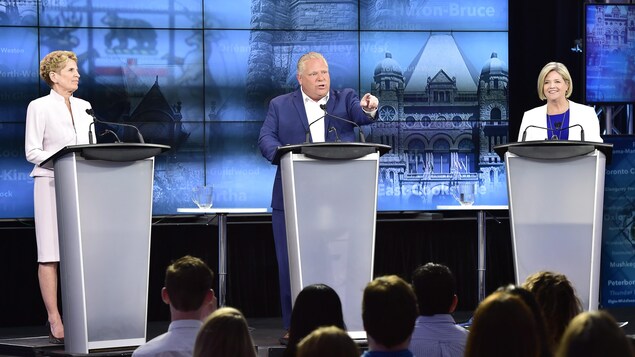 Le chef du Parti progressiste-conservateur de l'Ontario, Doug Ford (au centre), s'adresse à la foule. La première ministre sortante, à tête du Parti libéral de l'Ontario, Kathleen Wynne (à gauche) et la chef du Nouveau parti démocratique de l'Ontario, Andrea Horwath, attendent leur tour de parole.