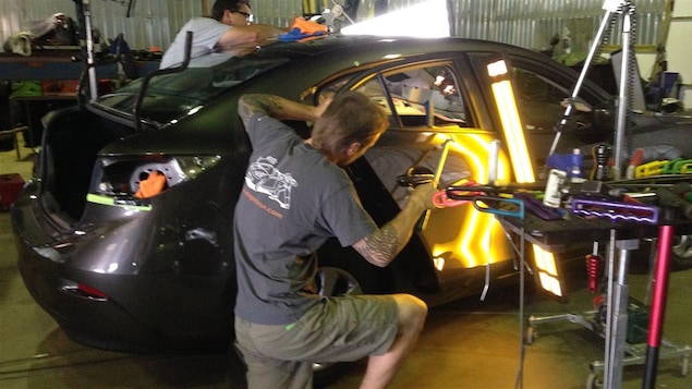 Deux débosseleurs sont en train de réparer la carrosserie d'un véhicule. Deux débosseleurs sont en train de réparer la carrosserie d'un véhicule.