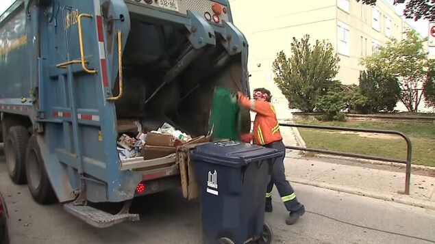 Photo d'un éboueur qui verse le contenu d'un bac vert dans un camion de collecte à Toronto.
