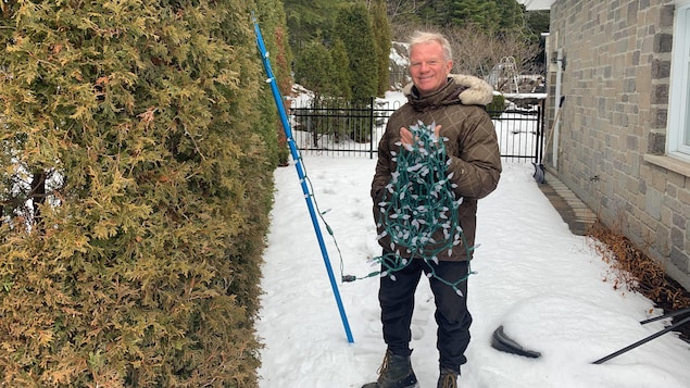 Un homme tient des lumières de Noël à l'extérieur de sa maison.