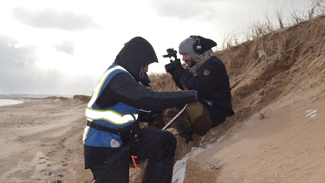 Deux personnes filment et prennent des mesures sur une dune de sable.