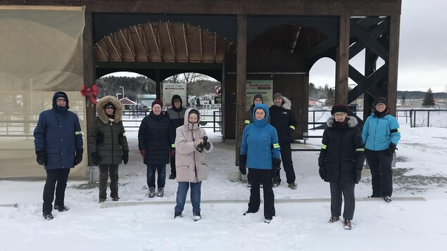 Une dizaine de personnes distancée posent sous un gazebo, l'hiver.