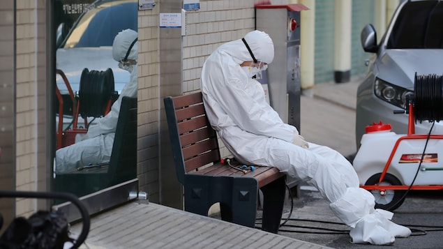Un travailleur médical en tenue de protection assis sur un banc.