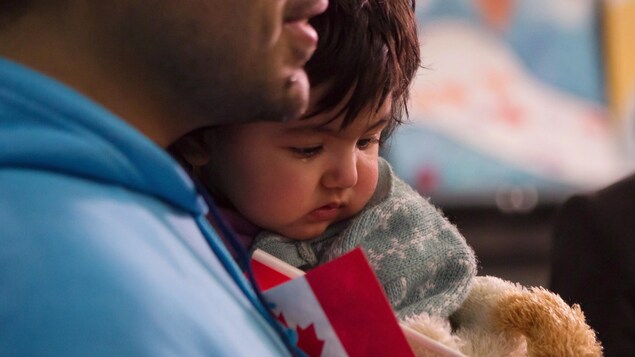 Une petite fille dans les bras de son père qui tient un petit drapeau canadien Une petite fille dans les bras de son père qui tient un petit drapeau canadien