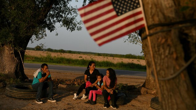 Un homme, une femme, une adolescente et une jeune fille attendent sur des pneus. Un drapeau des États-Unis flotte, accroché à un arbre.