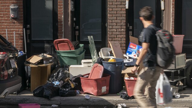 Un homme passe devant un amas de poubelles, de meubles et de déchets. 