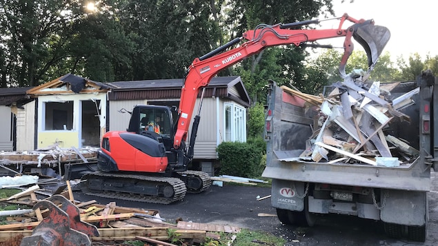 Une pelle mécanique démolit une maison mobile.