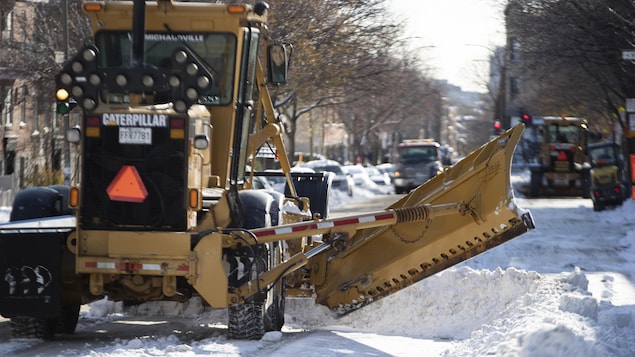 Des camions déneigent une rue de Montréal.