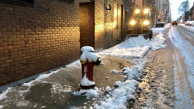 Un petit tracteur pousse la neige en bas du trottoir.