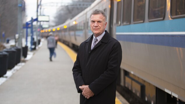 Le maire de Deux-Montagnes, Denis Martin, sur un quai avec un train en arrière plan.