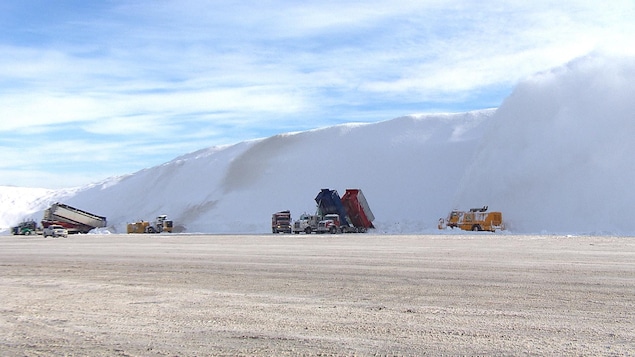Des camions vident leur chargement sur une montagne de neige.