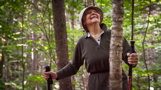 Francine, deux bâtons de marche aux mains, regarde le haut des arbres avec émerveillement
