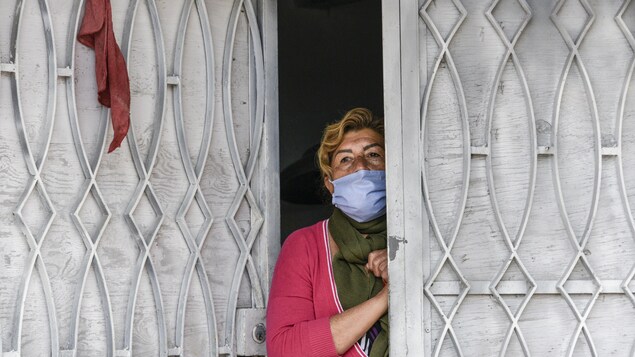 Une femme portant un masque facial attend à la porte de sa maison pour recevoir de l'aide alimentaire alors que les militaires colombiens visitent le bidonville appauvri du quartier d'El Codito distribuant des paniers alimentaires familiaux pendant la quarantaine obligatoire ordonnée par le gouvernement le 23 avril 2020 à Bogota, en Colombie. 