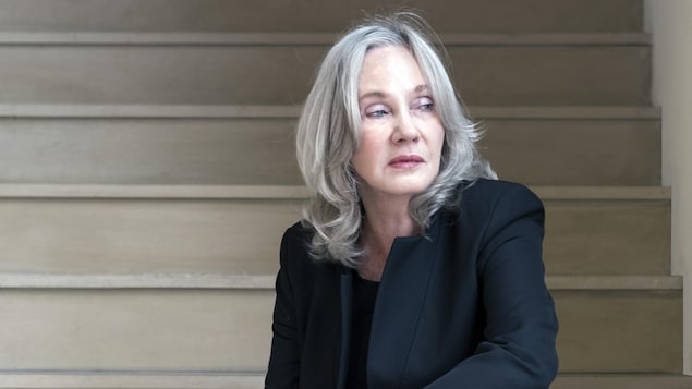 Assise sur une marche d'escalier, la diva jette un regard furtif vers sa droite. Elle est vêtue de vêtements noirs.