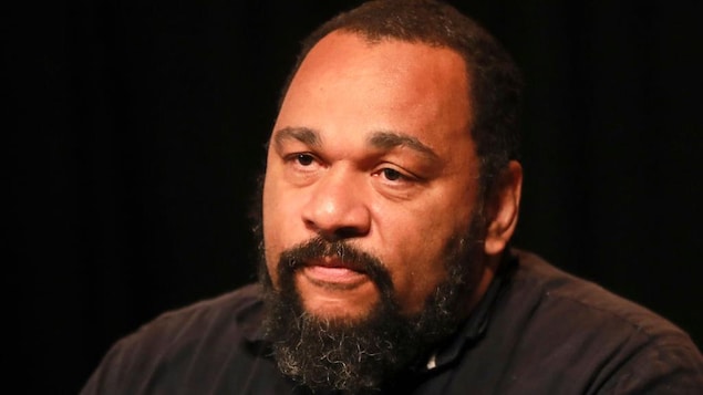Portrait de Dieudonné portant une chemise noire et une barbe.