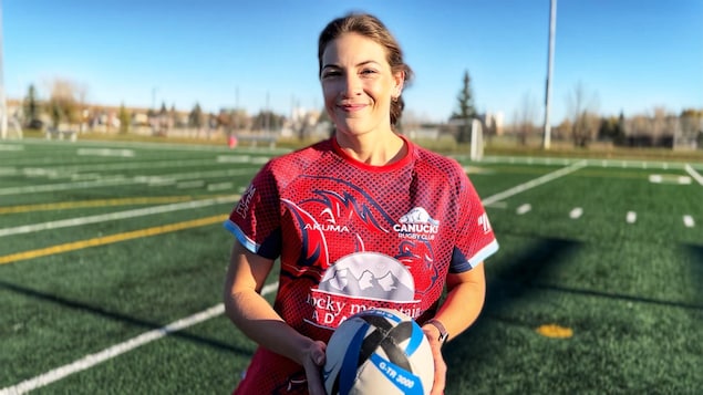 Une femme sur un terrain de football américain qui tient un ballon de rugby.