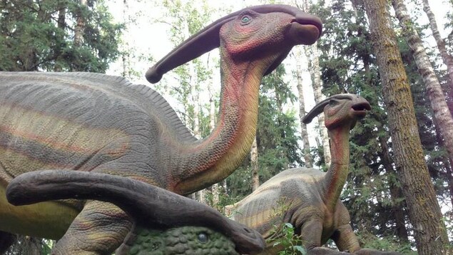 Trois dinosaures, dont un en avant-plan, se dressent dans la forêt, avec leurs écailles vertes et rouges. Trois dinosaures, dont un en avant-plan, se dressent dans la forêt, avec leurs écailles vertes et rouges.