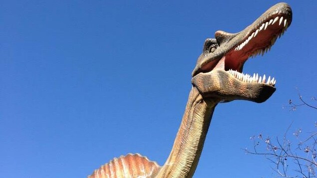 Un dinosaure se dresse en contre-plongée, gueule ouverte, parmi les arbres du parc thématique. Un dinosaure se dresse en contre-plongée, gueule ouverte, parmi les arbres du parc thématique.