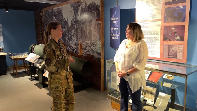 Des femmes dont une en uniforme de camouflage discutent devant le présentoir d'un musée. 