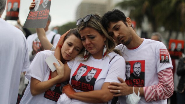 Trois personnes portant des t-shirts avec des images des deux personnes disparues s'enlacent pour se consoler.