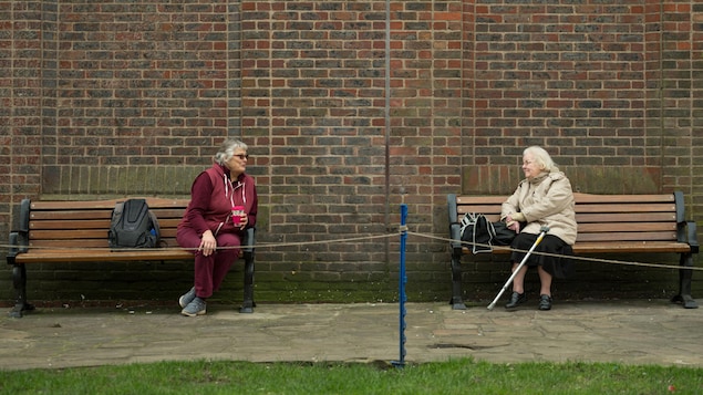 Deux dames âgées font la conversation assises sur deux bancs de parc séparés, à plus de deux mètres de distance l'une de l'autre, le 19 mars 2020 à York, en Angleterre.