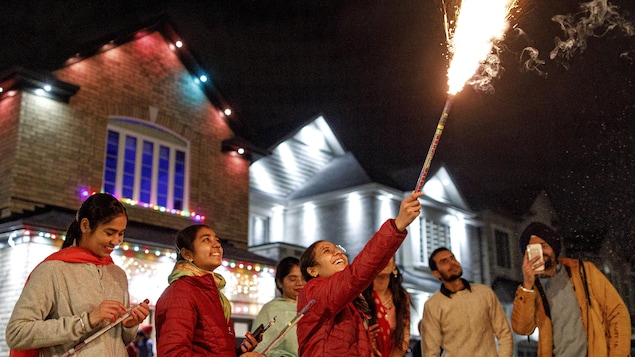 Une femme entourée de proches tient une baguette d'où sortent des feux d'artifice.